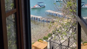 Vista desde una ventana sobre aguas tranquilas, con barcos, un muelle y una pequeña mesa y sillas de madera.