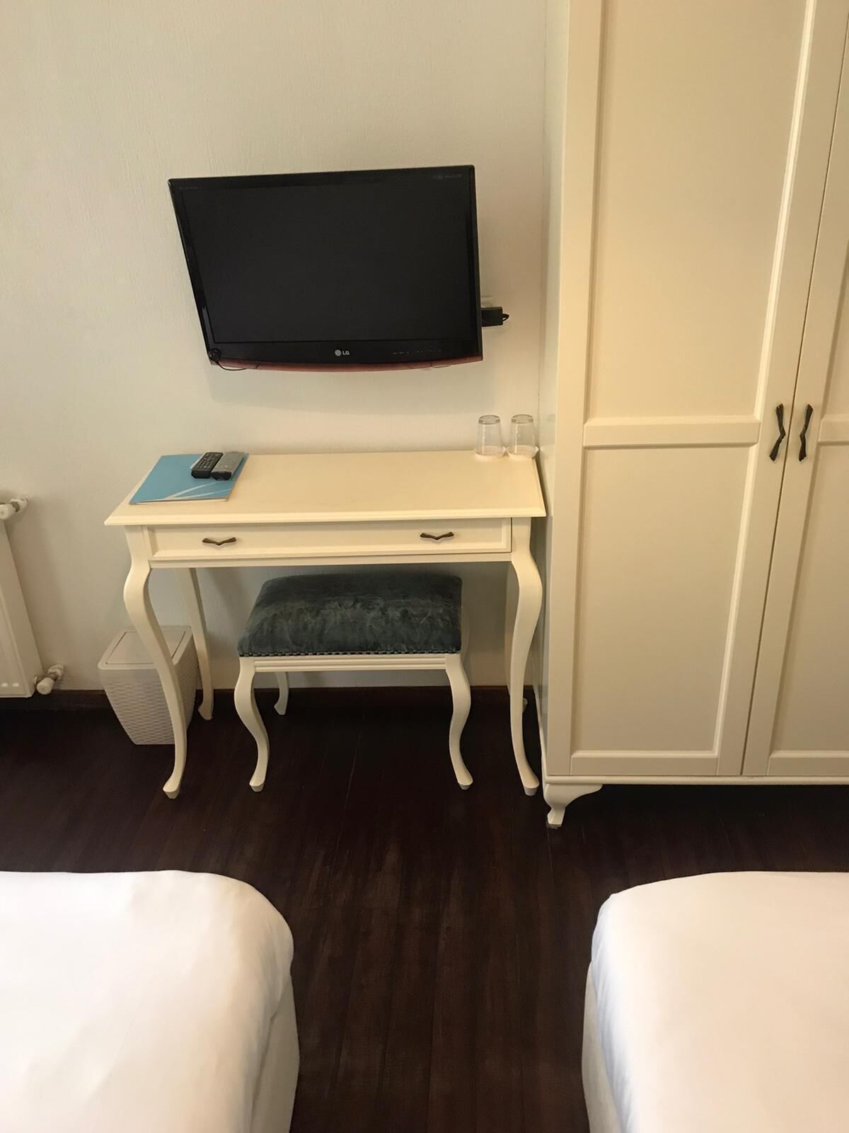 A room with a white desk, a television mounted above it, a cabinet, and two beds.