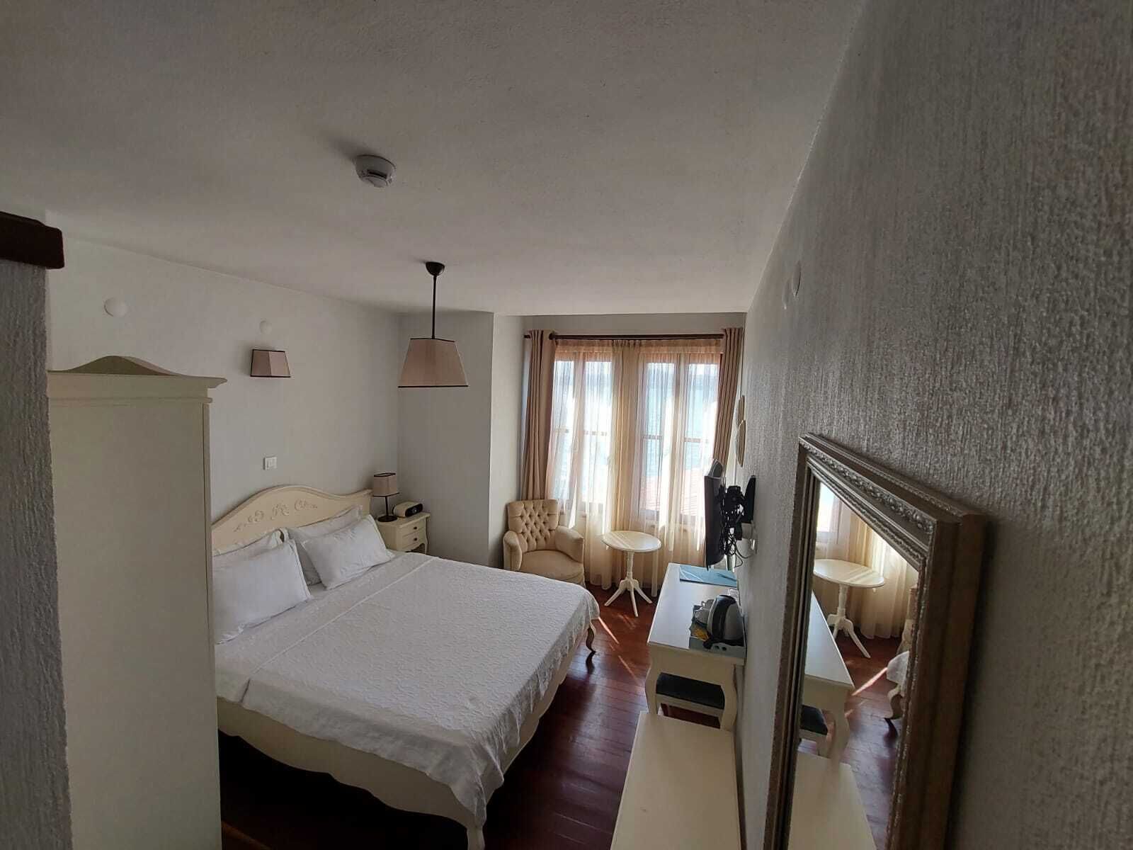 Habitación de hotel con cama, mesitas de noche, una silla, una pequeña mesa, un espejo y una ventana con cortinas.