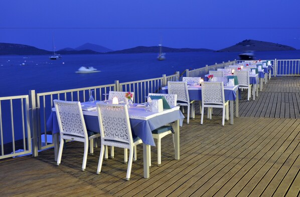 Un comedor con mesas y sillas en una terraza de madera con vista al mar.