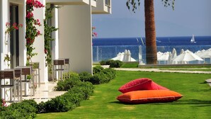 A modern building with a clear view of the sea, a palm tree, and a well-maintained lawn with outdoor seating.