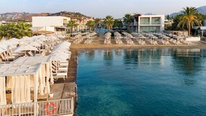 A waterfront resort with multiple sun loungers and umbrellas, a pool, and a lifebuoy on a dock.