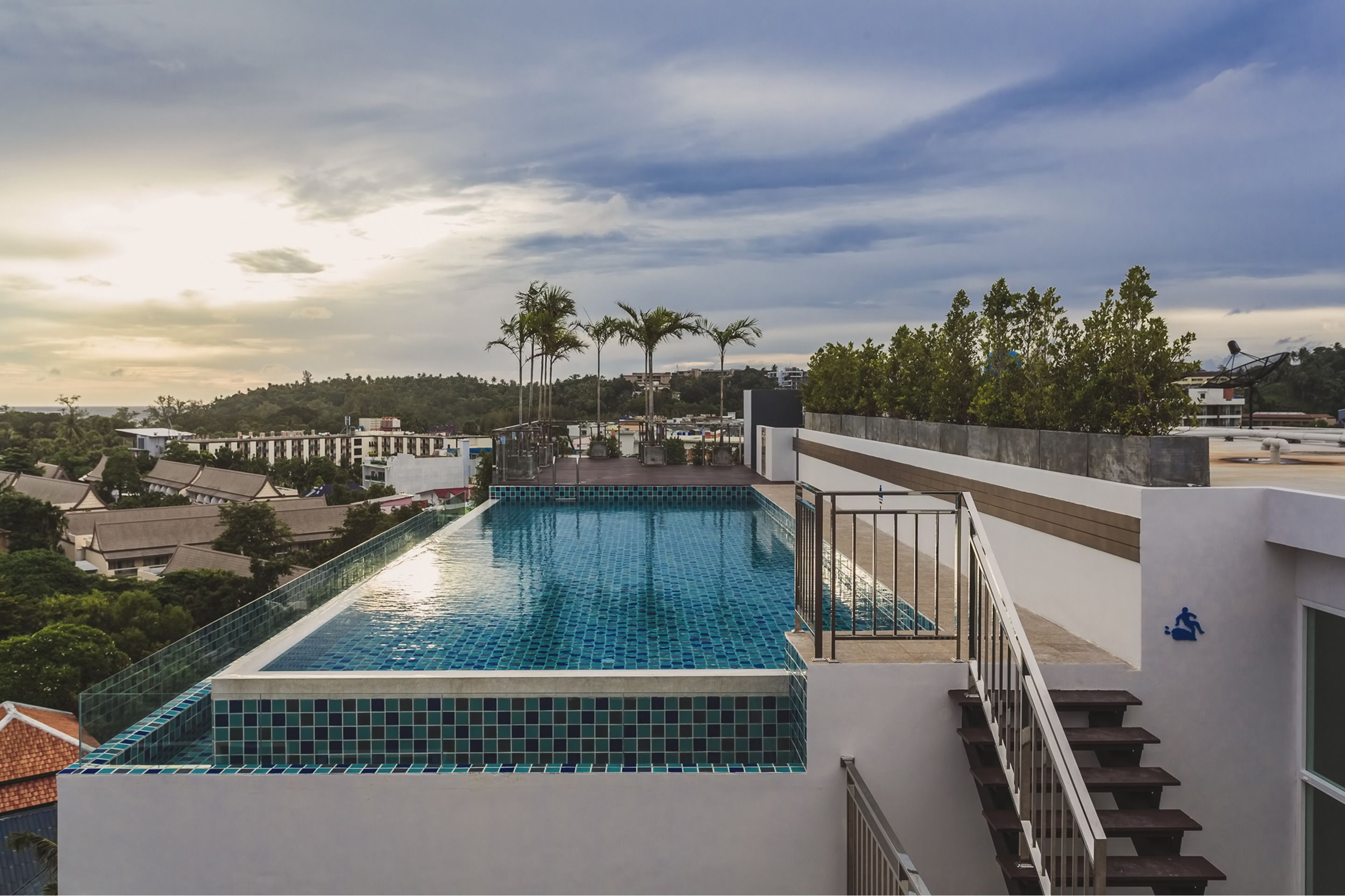 A rooftop swimming pool with a view of the surrounding area, including palm trees and buildings.