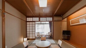 Ein traditioneller japanischer Raum mit Tatami-Böden, einem niedrigen Tisch mit Kissen und einer Schiebetür zu einem Balkon.