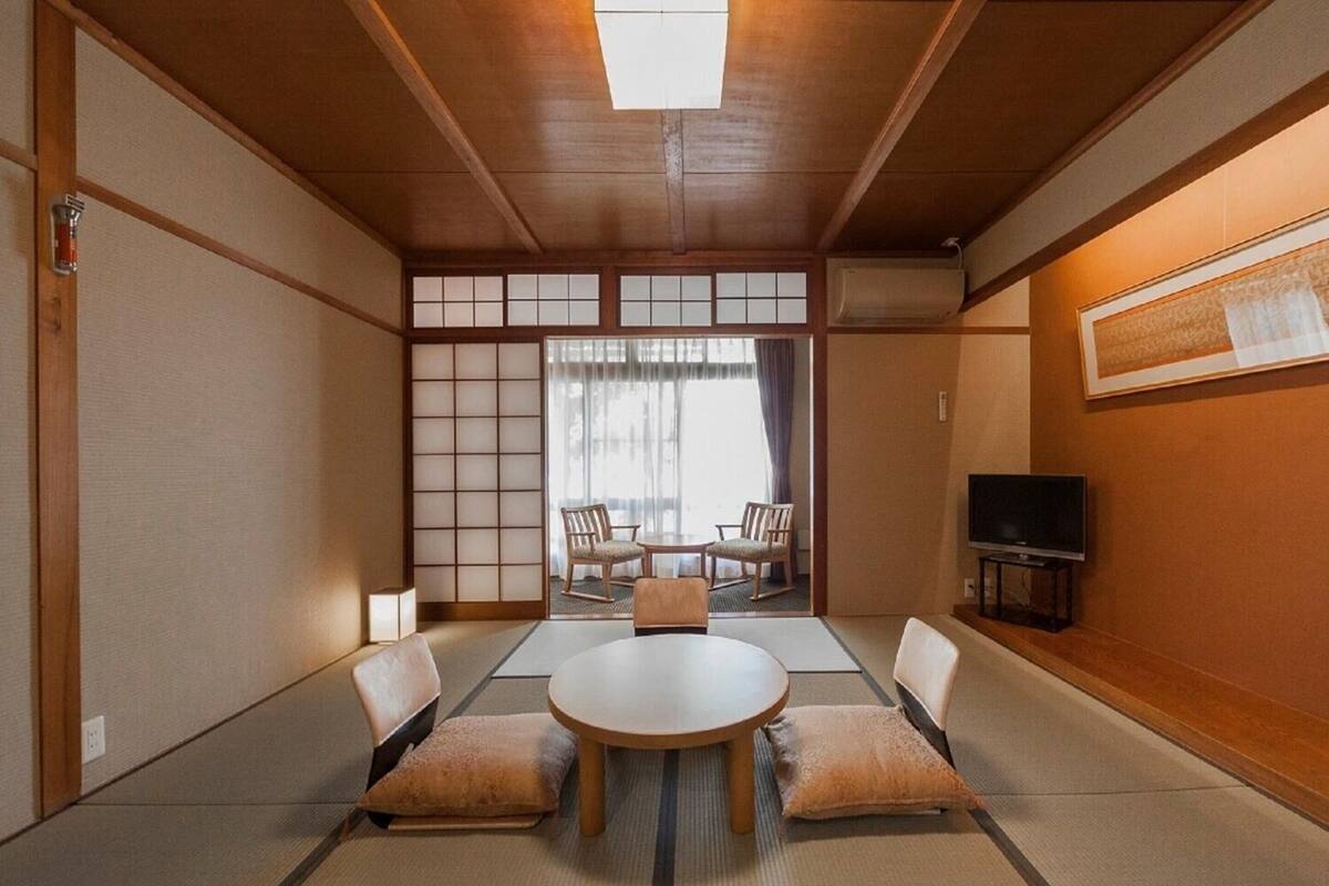 Ein traditioneller japanischer Raum mit Tatami-Böden, einem niedrigen Tisch mit Kissen und einer Schiebetür zu einem Balkon.
