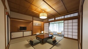 Ein traditioneller japanischer Raum mit Tatami-Böden, einem niedrigen Holztisch und einem Fernseher auf einem Schrank.
