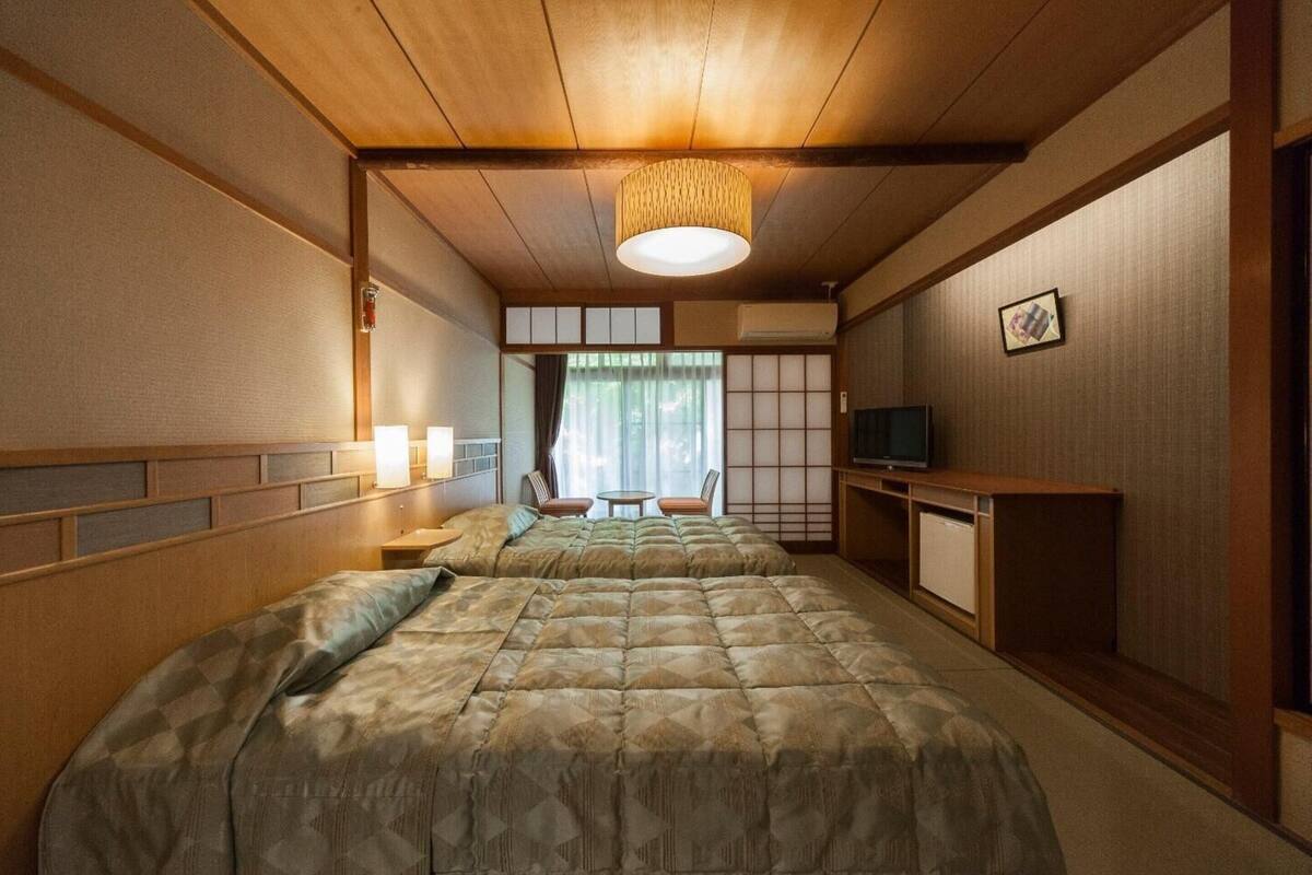 Ein traditionell eingerichtetes Hotelzimmer im japanischen Stil mit einem großen Bett, einem Fernseher, einem kleinen Tisch und Blick ins Freie durch eine Schiebetür.