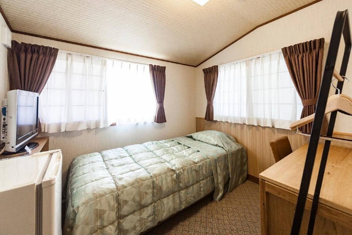 Ein kleines Zimmer mit Bett, Schreibtisch, Stuhl und Fernseher.