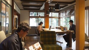 Ein modernes Interieur mit Holzmöbeln, einem großen Tisch und einer Sitzecke mit Blick durch große Fenster.