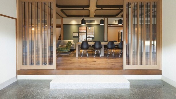 Ein modernes Interieur mit Essbereich, ausgestattet mit einem Holztisch, Stühlen, einer Couch und einer Treppe zu einer weiteren Ebene.