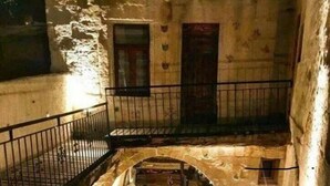 A dimly lit, narrow alleyway with a stone wall and metal railings, leading to a small courtyard with a bench and a door. - Sandik Cave Hotel (Ürgüp)