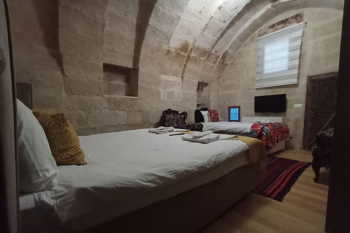 A room with a large bed, a small window, a television, and a wooden floor.