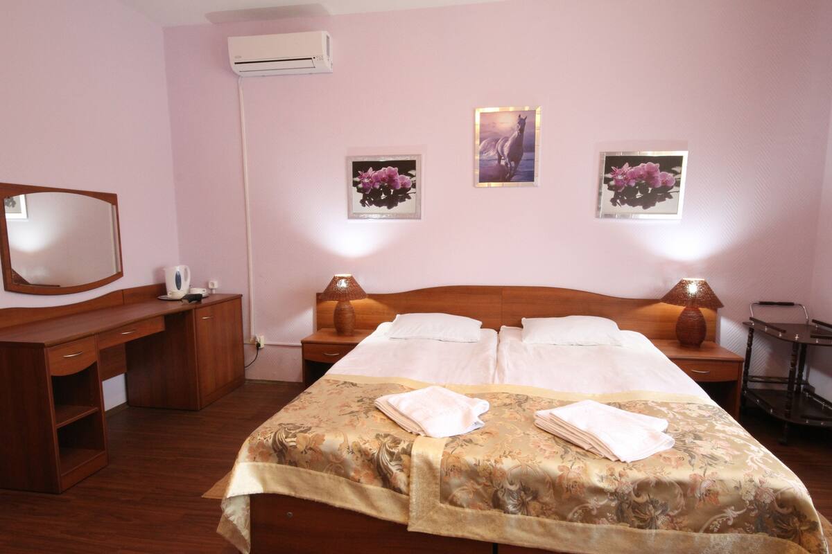 Hotellihuone, jossa on puinen sänky, kaksi yöpöytää valaisimineen, työpöytä, tuoli ja peili.