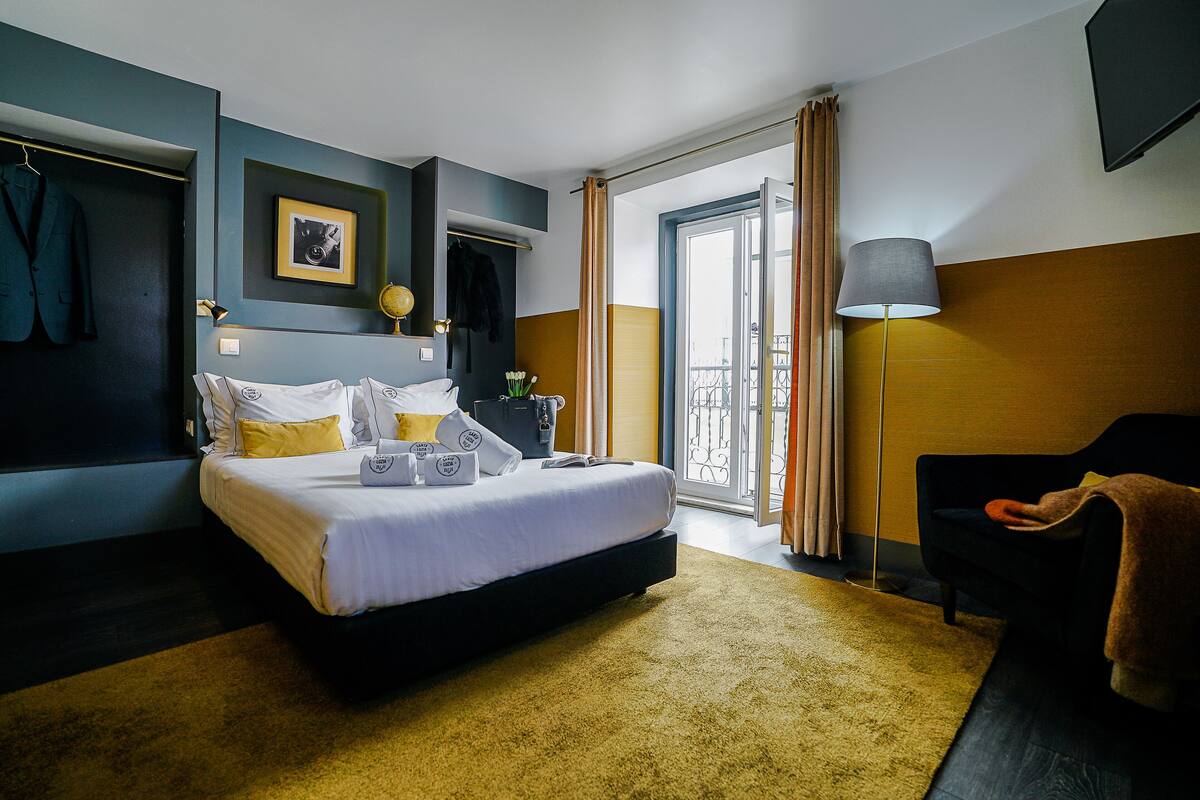Ein Hotelzimmer mit Bett, Schreibtisch, Stuhl, Lampe und Blick ins Freie.