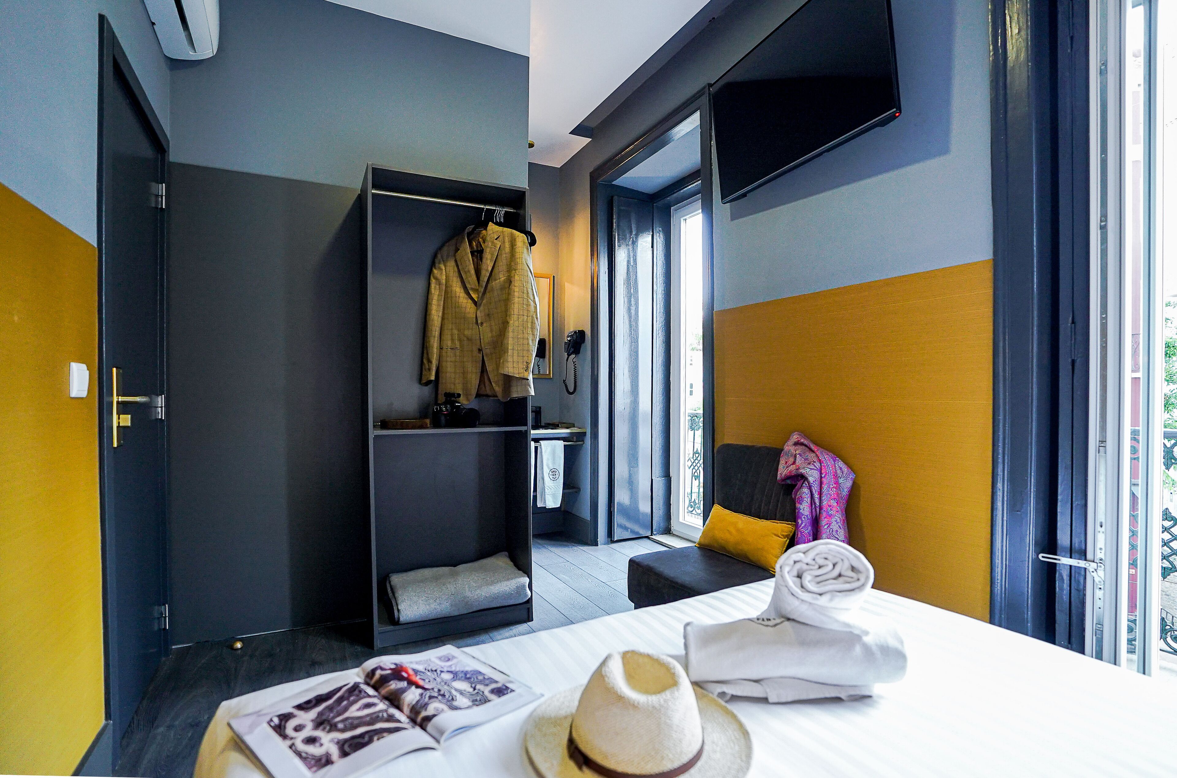 A modern hotel room with a bed, a desk, a wardrobe, and a view of the outdoors.
