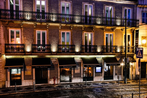 A row of restaurants with outdoor seating, a cobblestone street, and a train track in the foreground.