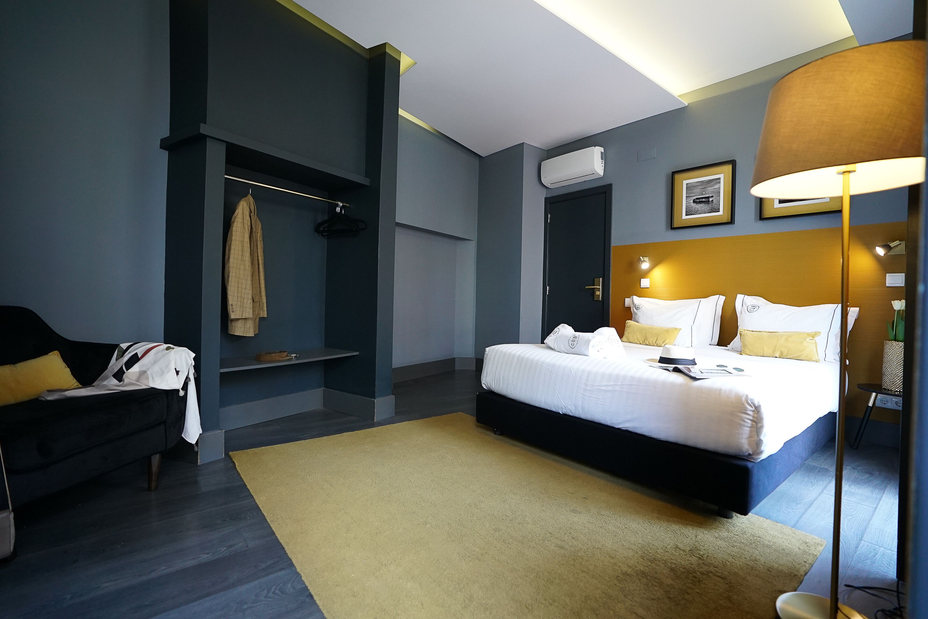 Una habitación de hotel moderna con una cama, un sofá, un perchero y una mesita de noche.