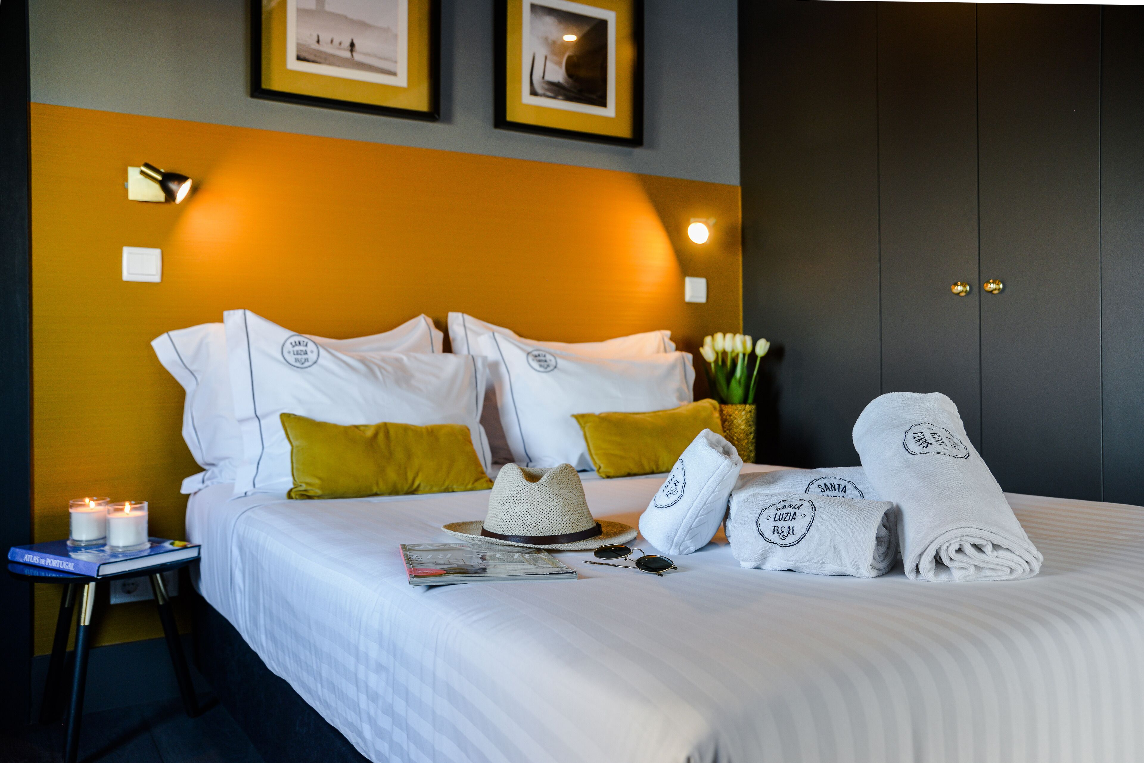 A neatly made bed with white linens, a straw hat, sunglasses, and a magazine on a bedside table.