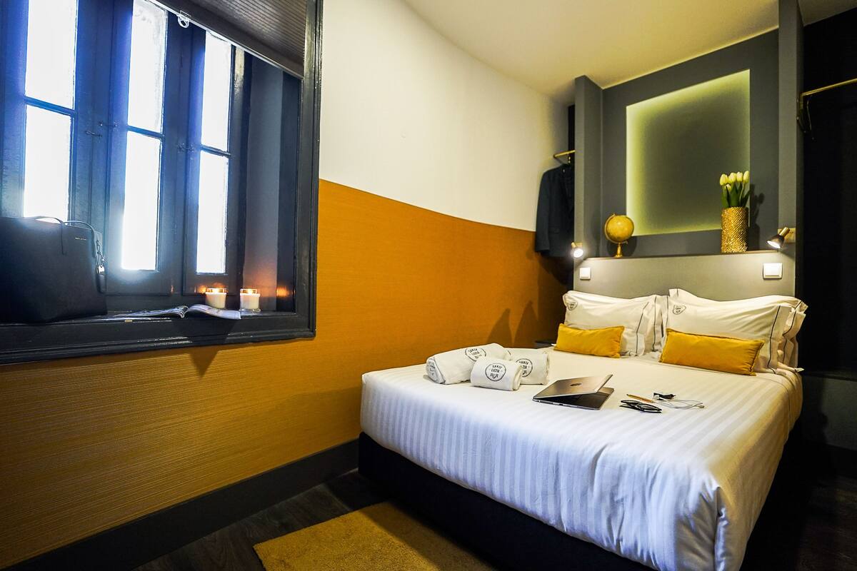 Ein Hotelzimmer mit Bett, Nachttisch, einem Fenster mit Vorhängen und einem an der Wand montierten Fernseher.