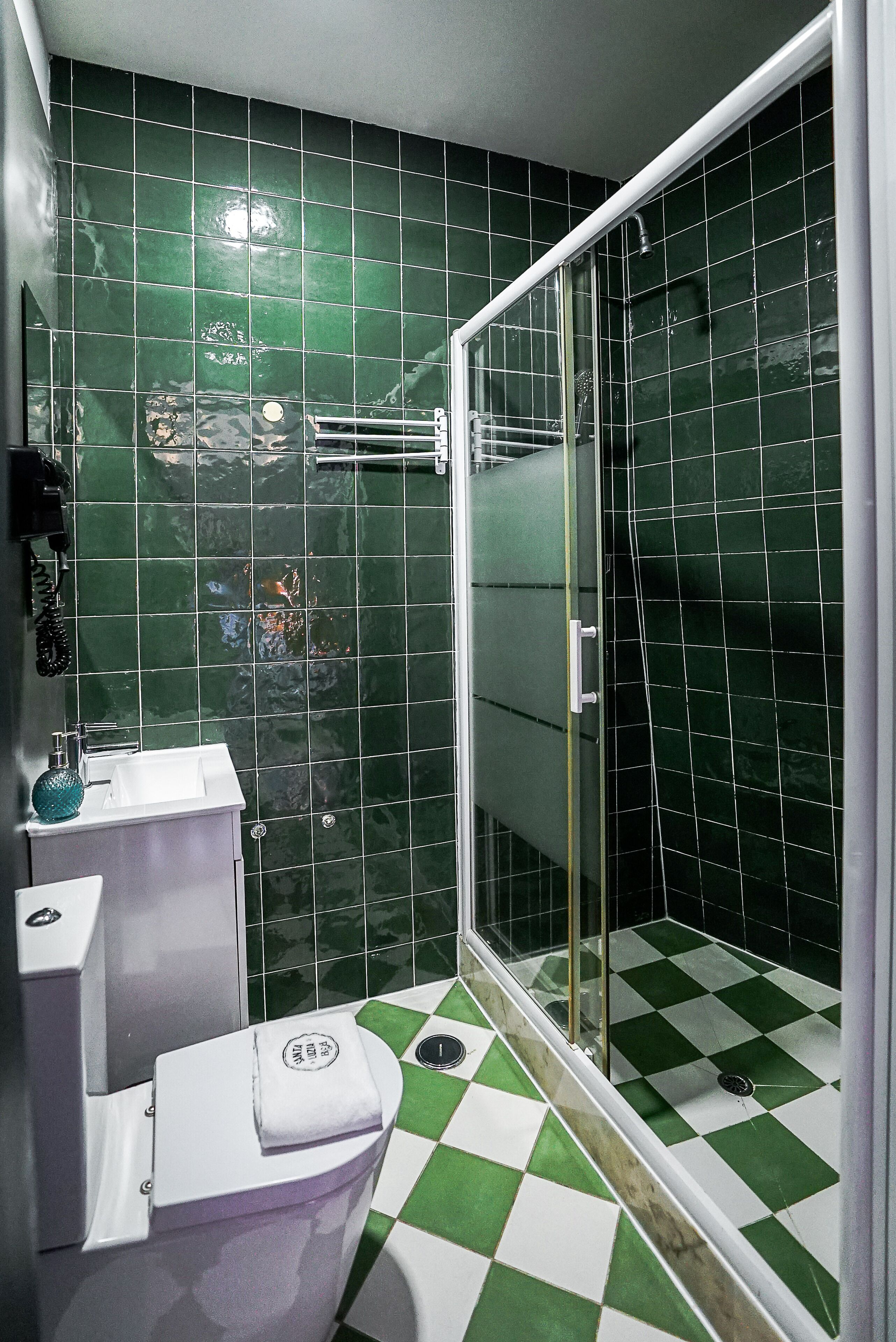 A bathroom with green tiles, a shower with a glass door, and a toilet.