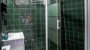 A bathroom with green tiles, a shower with a glass door, and a toilet.
