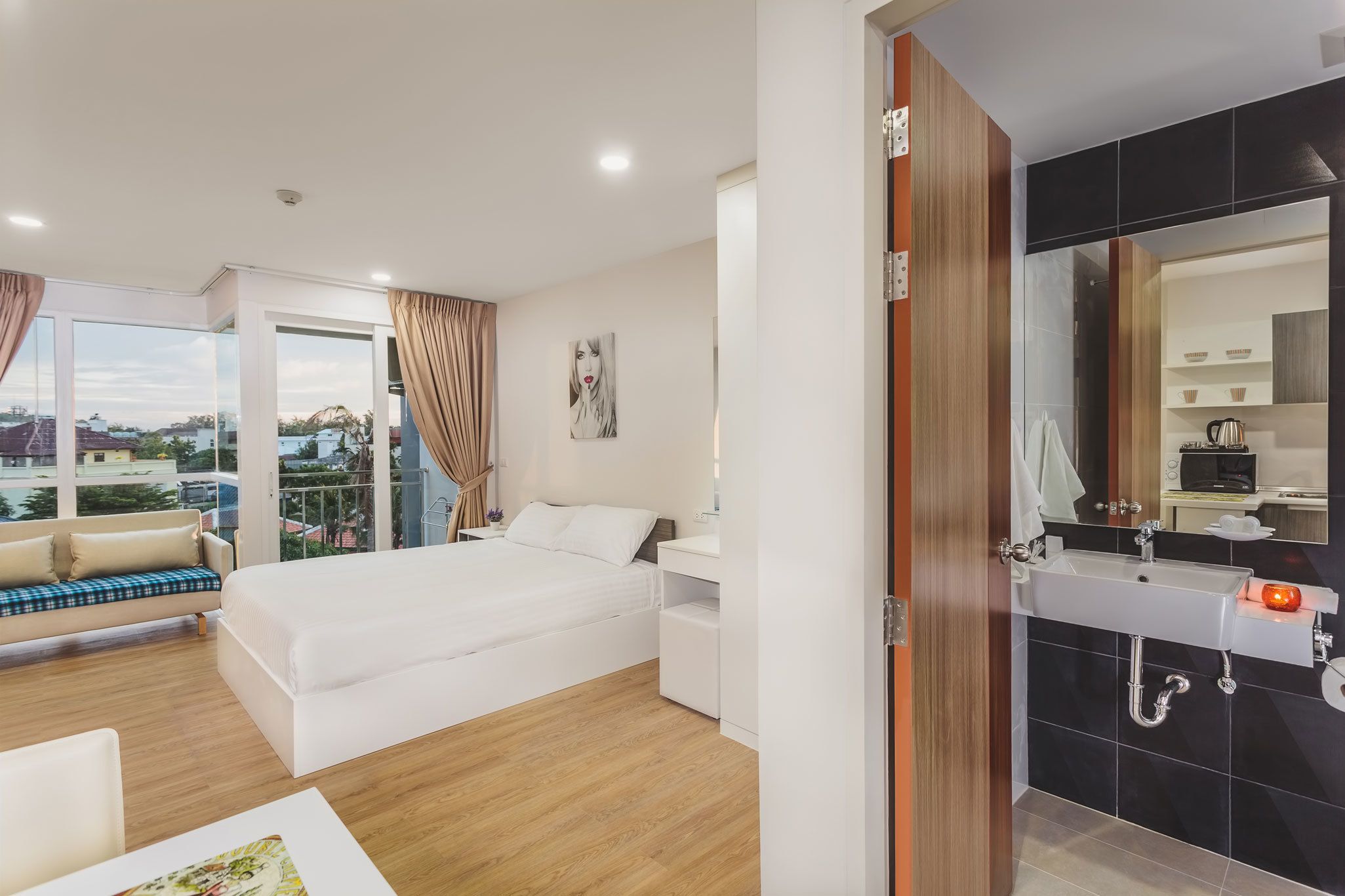 Una camera d'hotel moderna con un letto grande, un divano, un tavolo da pranzo e un bagno con lavandino e specchio.