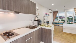 A modern kitchen with a built-in stove, a sink, and a microwave. There is a dining area with a sofa and a view of the city. - Condo in Kata in Ozone - A519 (Karon)