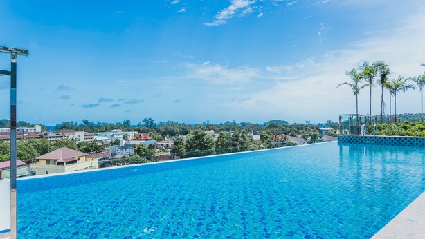 A clear blue swimming pool with a view of a residential area and palm trees in the background. - Condo in Kata in Ozone - A519 (Karon)