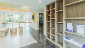 A modern reception area with a wooden reception desk, a seating area with two chairs, and a large wooden shelving unit with documents. - Condo in Kata in Ozone - A604 (Karon)