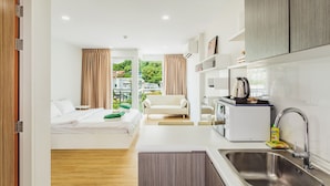 A compact hotel room with a bed, kitchenette, and a view of greenery. - Condo in Kata in Ozone - A604 (Karon)