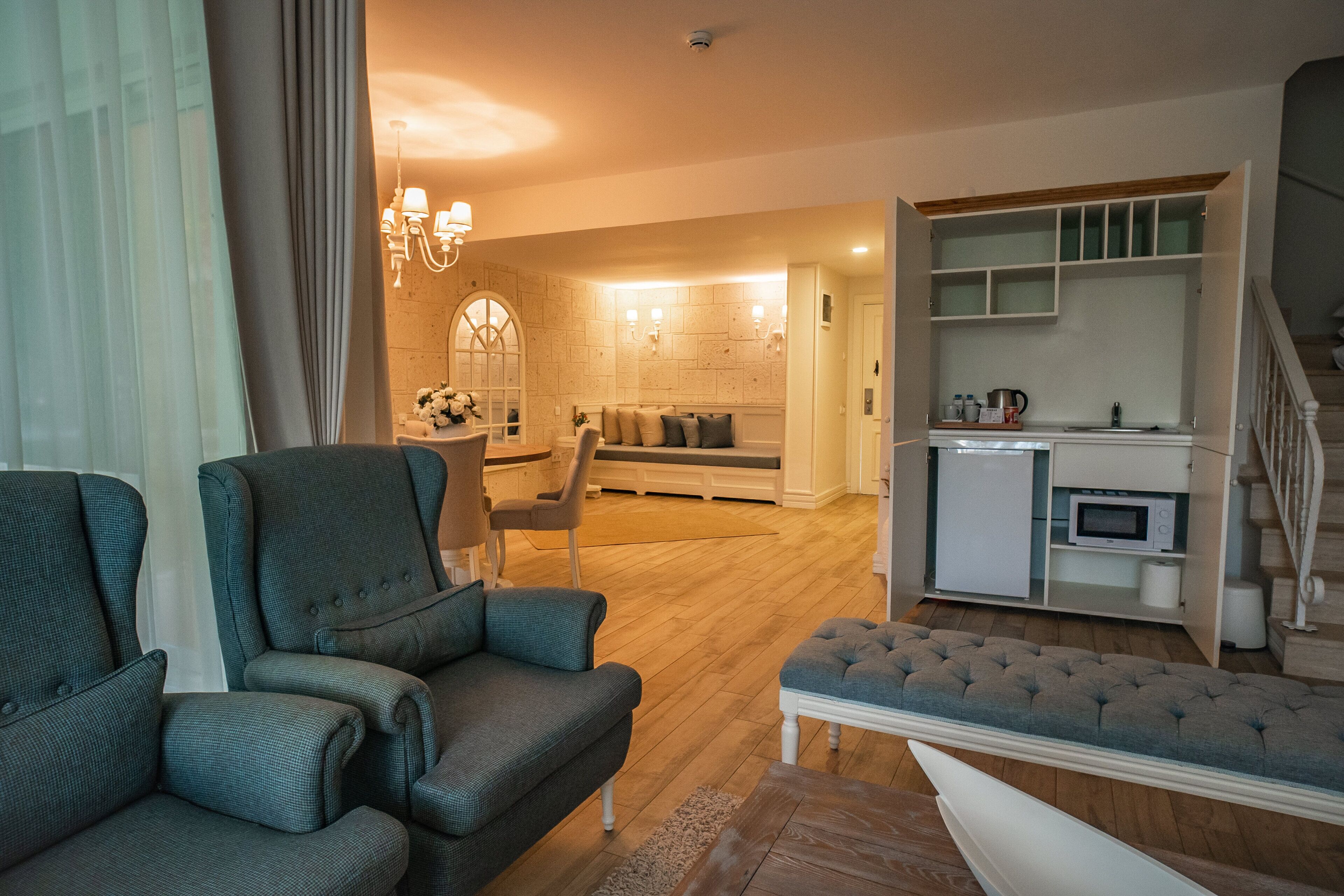 Una sala de estar moderna con un sofá, un sillón y un otoman, un comedor con una mesa y sillas, y una cocina con microondas y refrigerador.