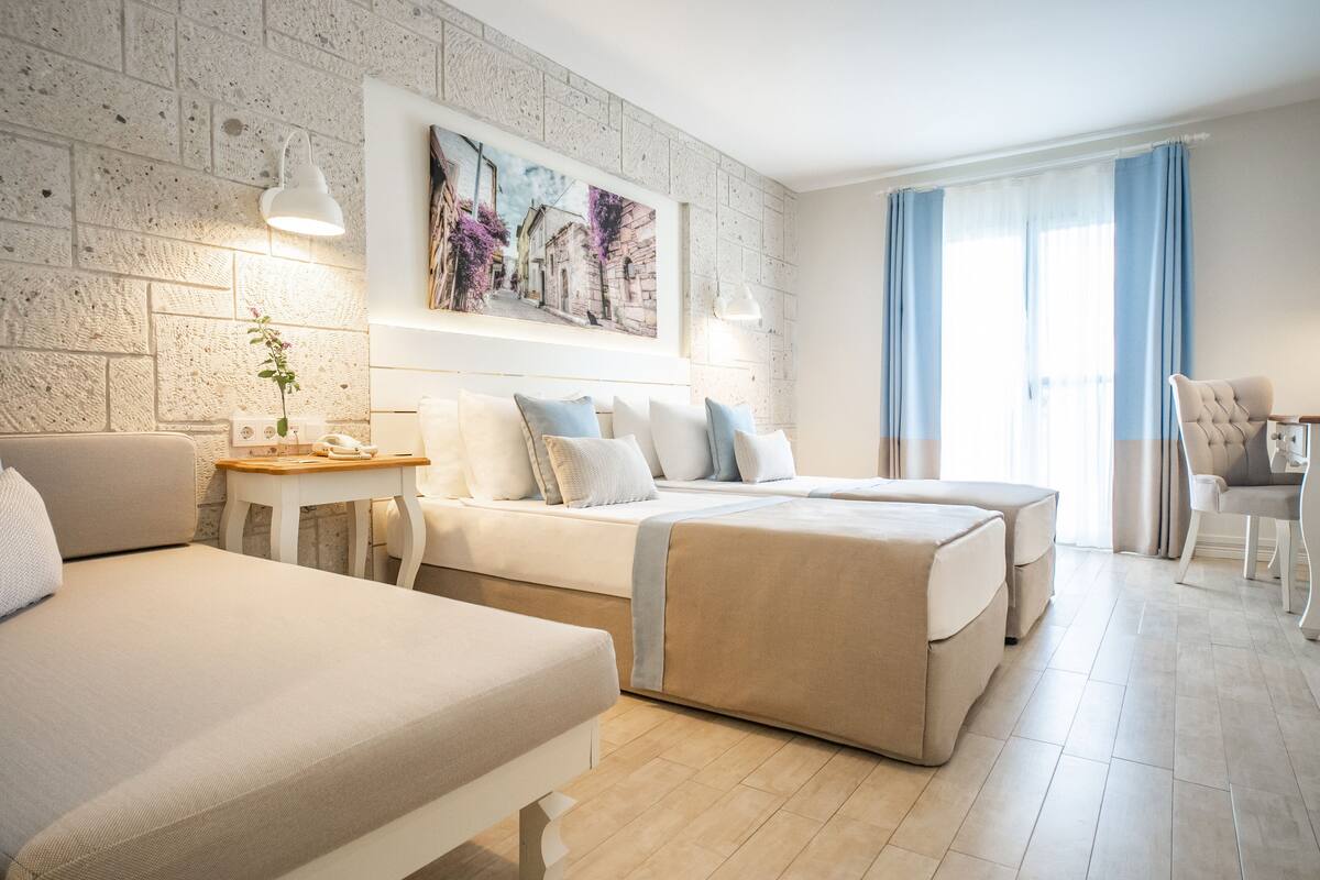 Ein Hotelzimmer mit zwei Betten, einem kleinen Tisch mit einer Vase, einem Sessel und einem Bild an der Wand.