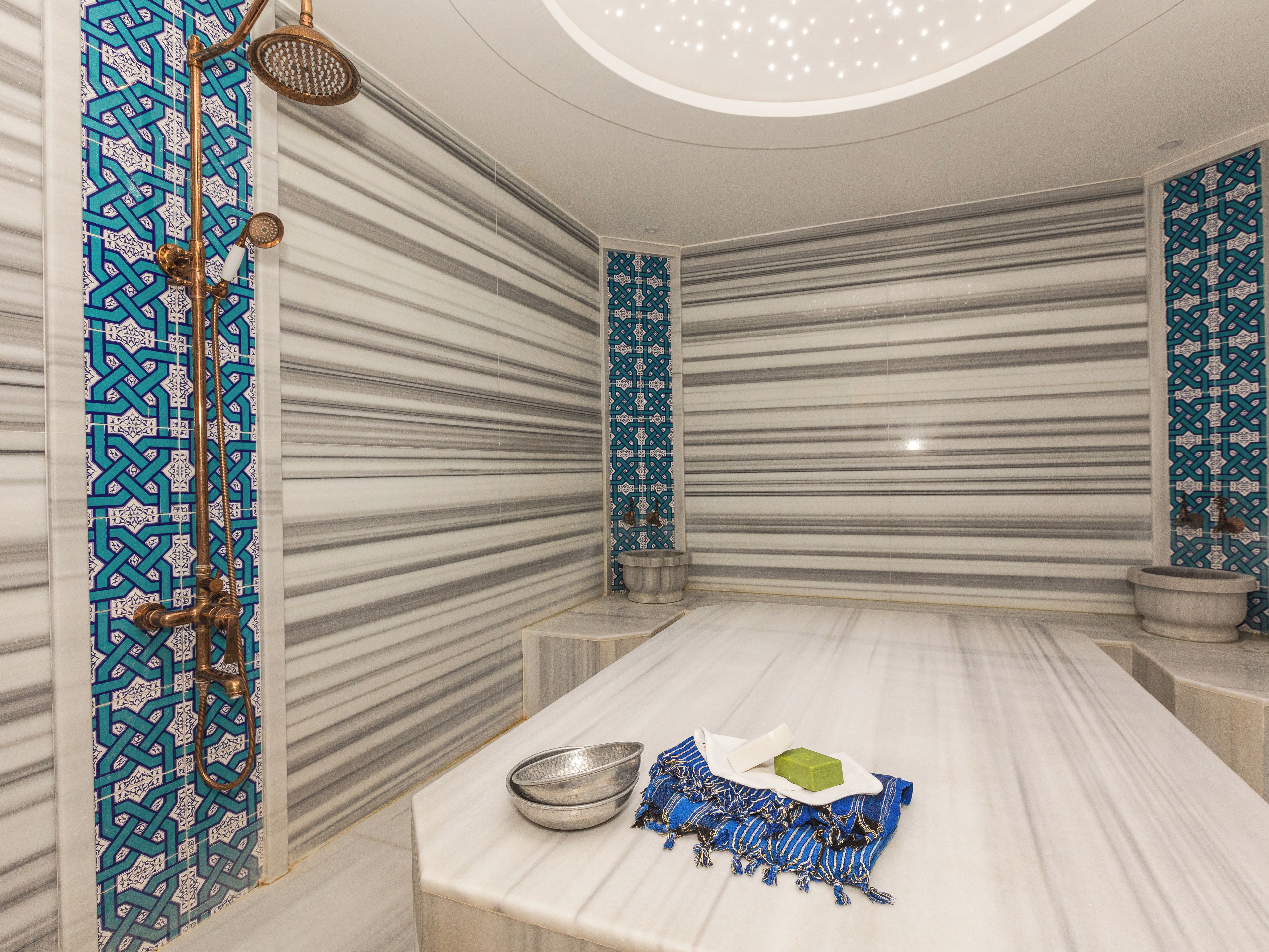 Ein Badezimmer mit Marmorwaschtisch, einer Dusche mit blau gefliesten Wänden und einer Decke mit einer runden Leuchte.