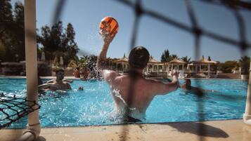 Piscina cercada por uma rede, com água azul cristalina e uma pessoa brincando com uma bola.