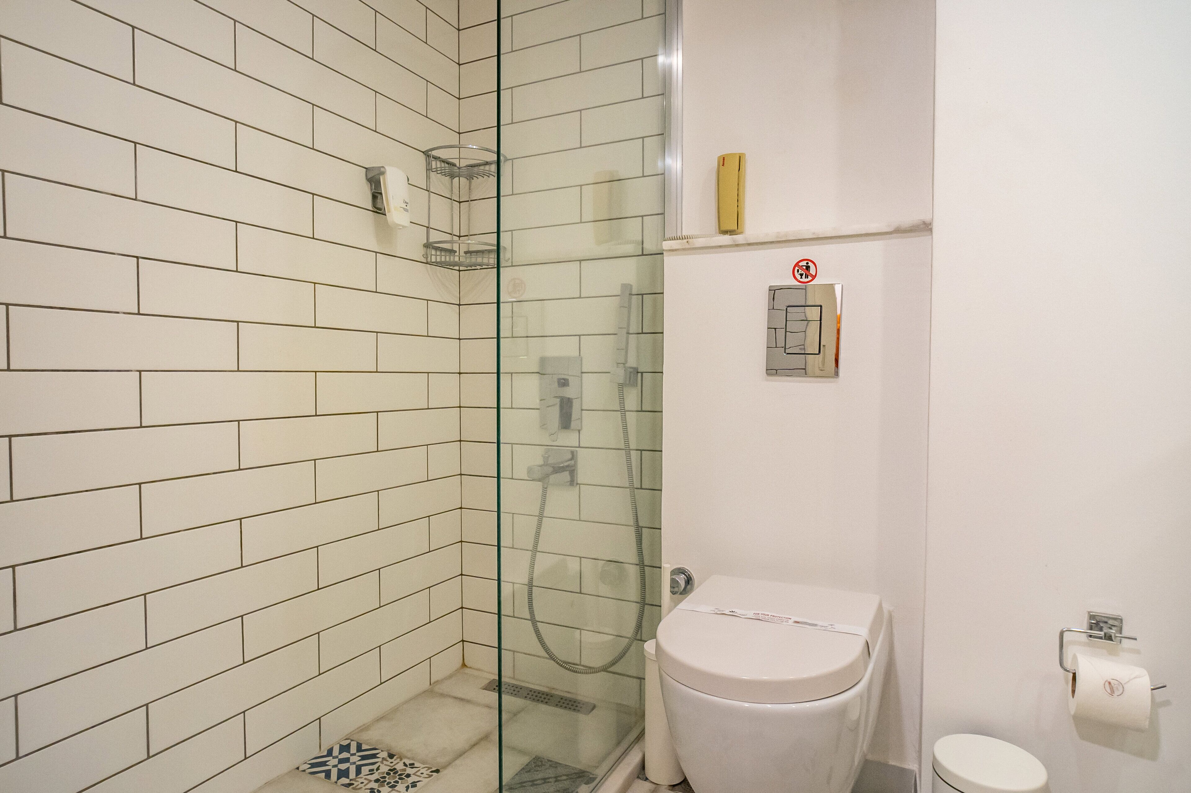 A bathroom with white tiled walls, a glass shower enclosure, a toilet, and a small shelf with a telephone.