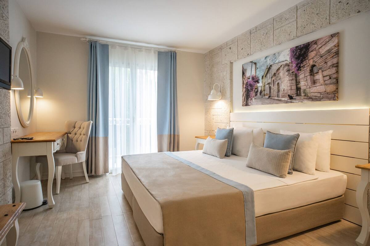 Ein modernes Hotelzimmer mit einem großen Bett, einem Schreibtisch, einem Sessel und einem Gemälde an der Wand.