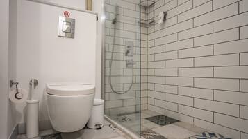 Un baño con inodoro, bidé y cabina de ducha con mampara de vidrio.