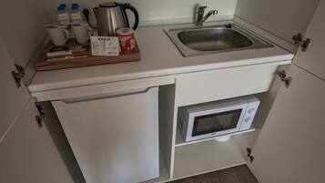 A compact kitchenette with a sink, microwave, and a wooden tray with kitchen items.