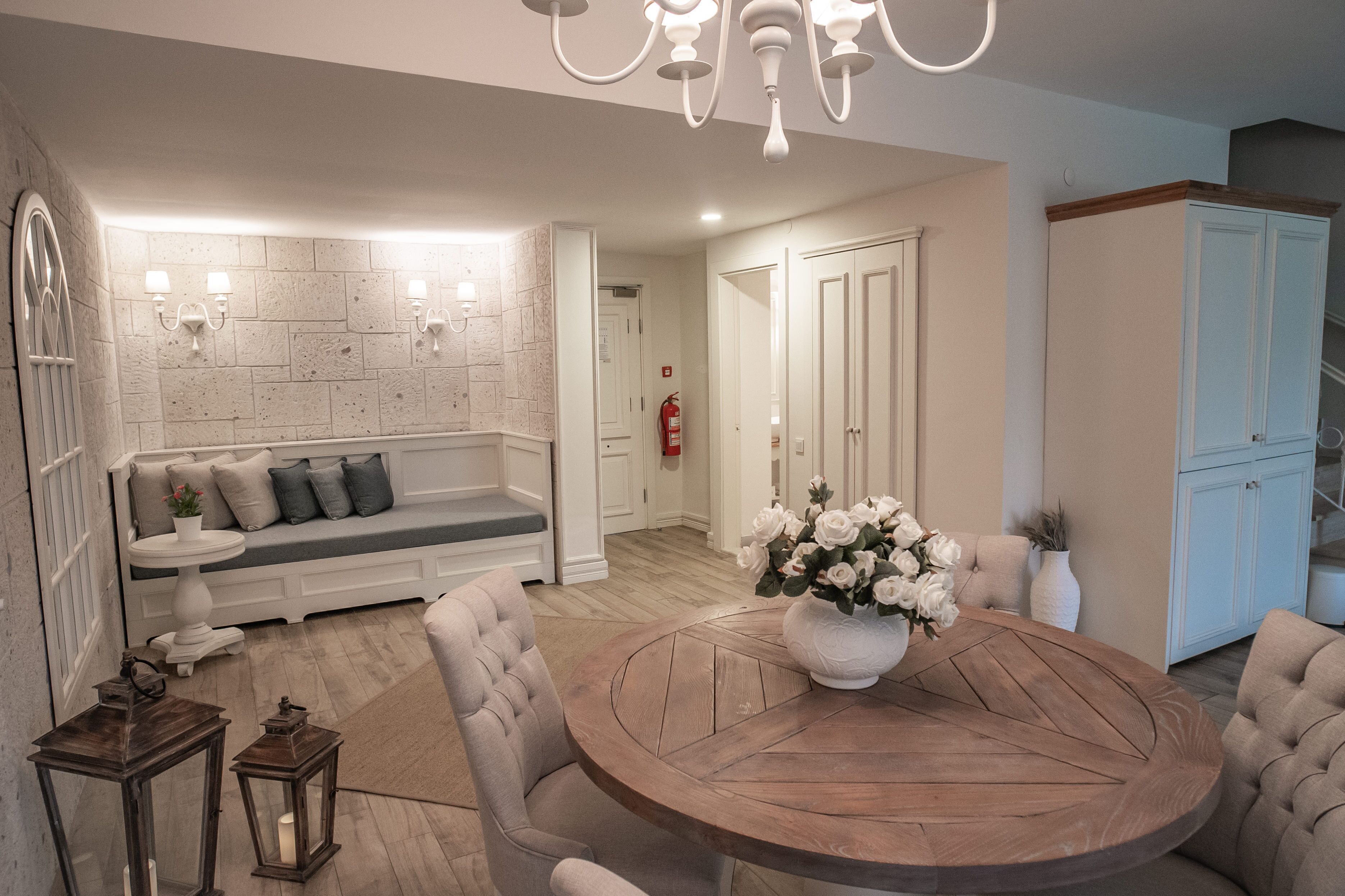 Ein modernes Wohnzimmer mit einem runden Holztisch, einem weißen Sofa mit grauen Kissen und einer weißen Vase mit Blumen.