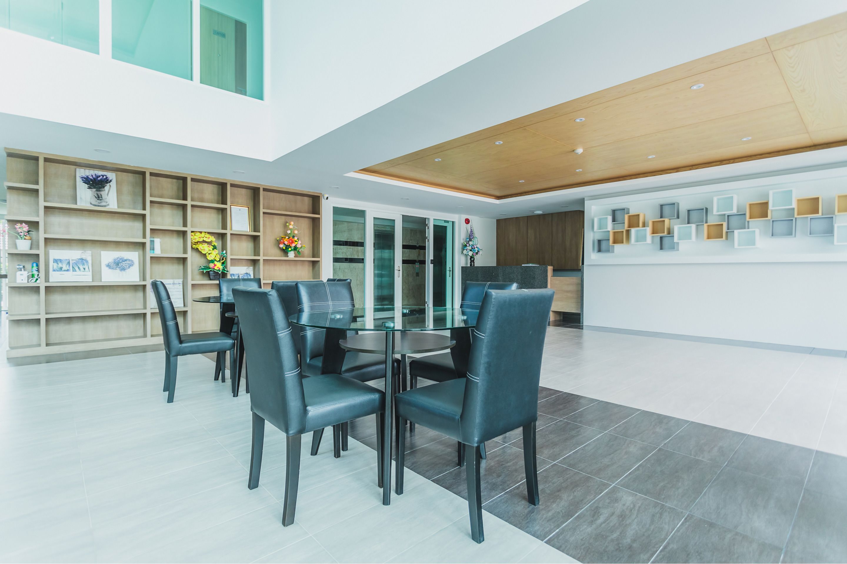A modern dining area with a glass table and black chairs, surrounded by wooden shelves with decorative items.