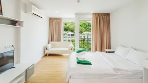 A modern hotel room with a bed, a sofa, a TV, and a balcony with curtains. - Condo in Kata in Ozone - Unit A606 (Karon)