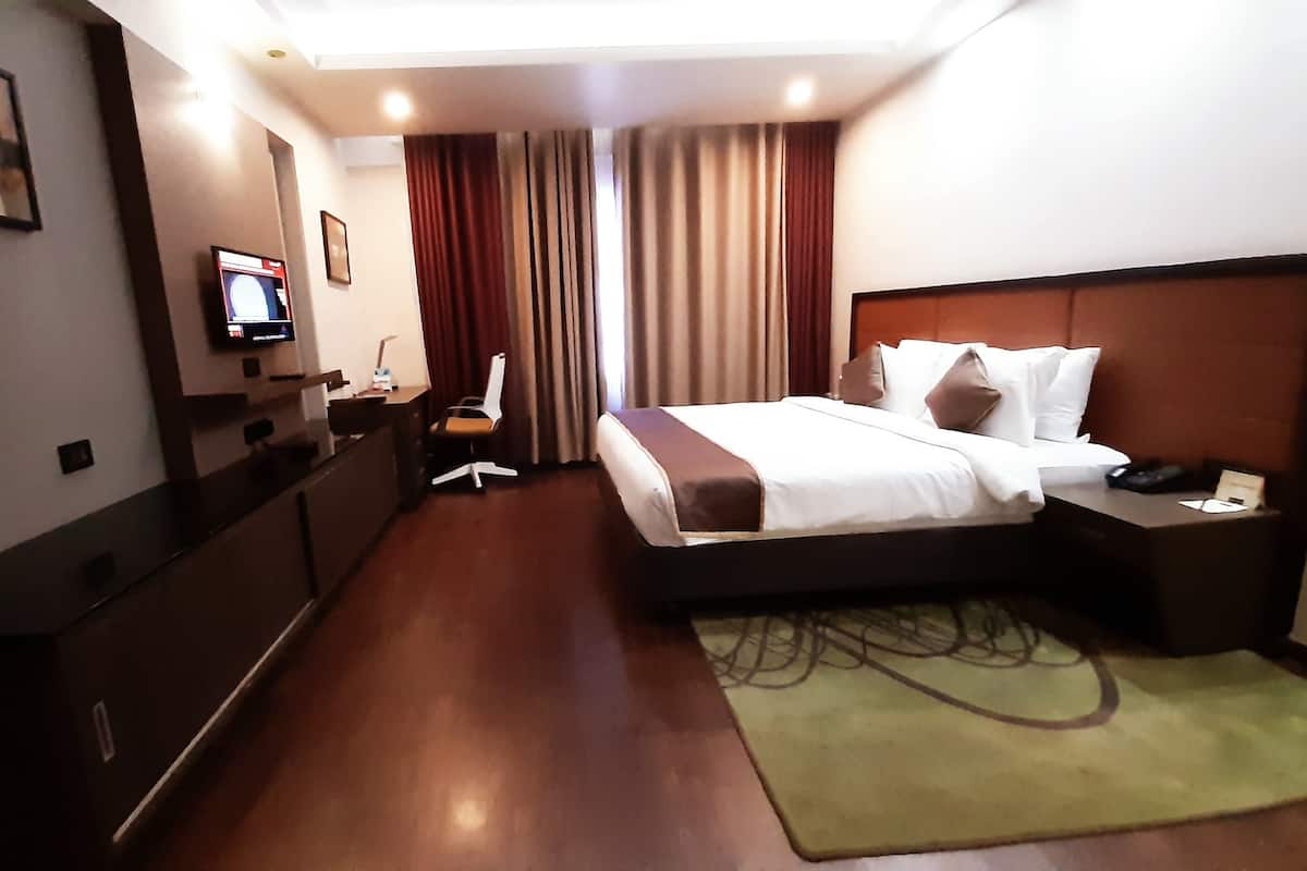 A hotel room with a bed, a desk, a chair, a television, and a window with curtains.