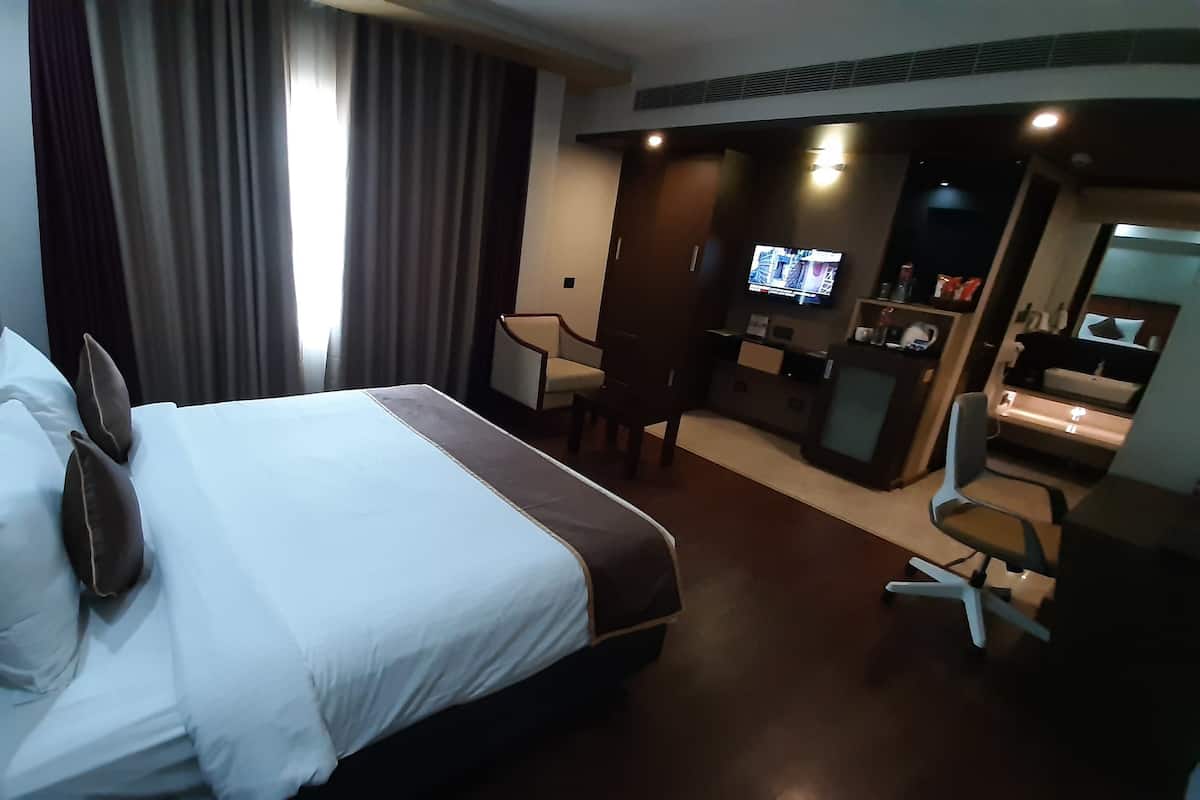 A hotel room with a large bed, a desk with a chair, a television, and a minibar.