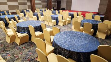 Un salón de conferencias con mesas y sillas redondas, un escenario y una pantalla de proyector.