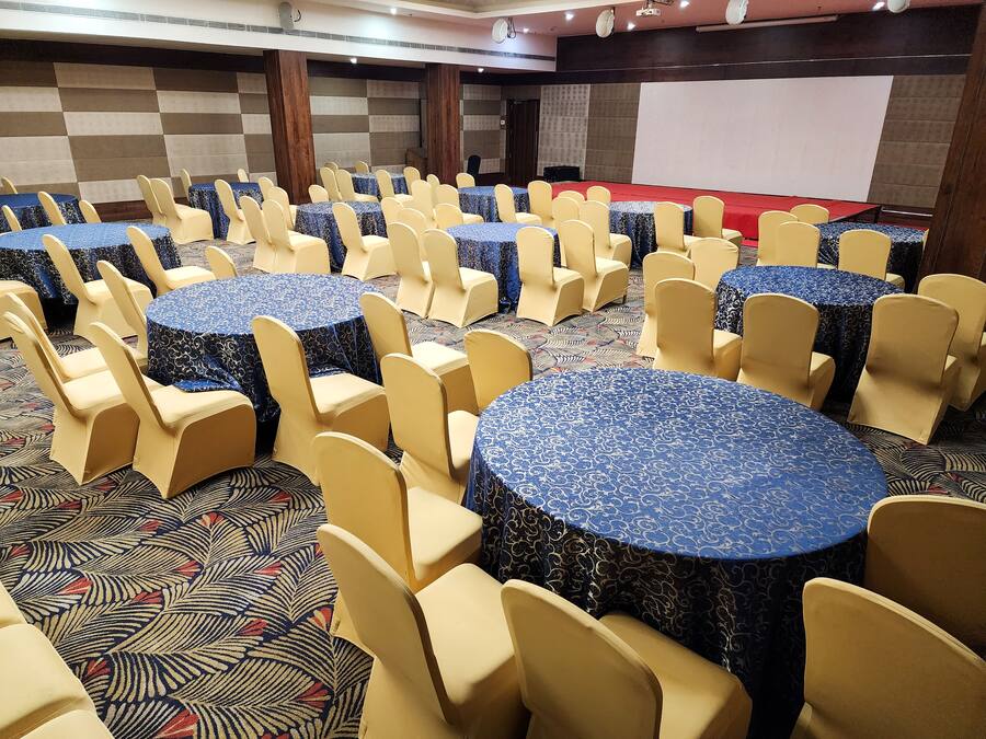 Un salón de conferencias con mesas y sillas redondas, un escenario y una pantalla de proyector.