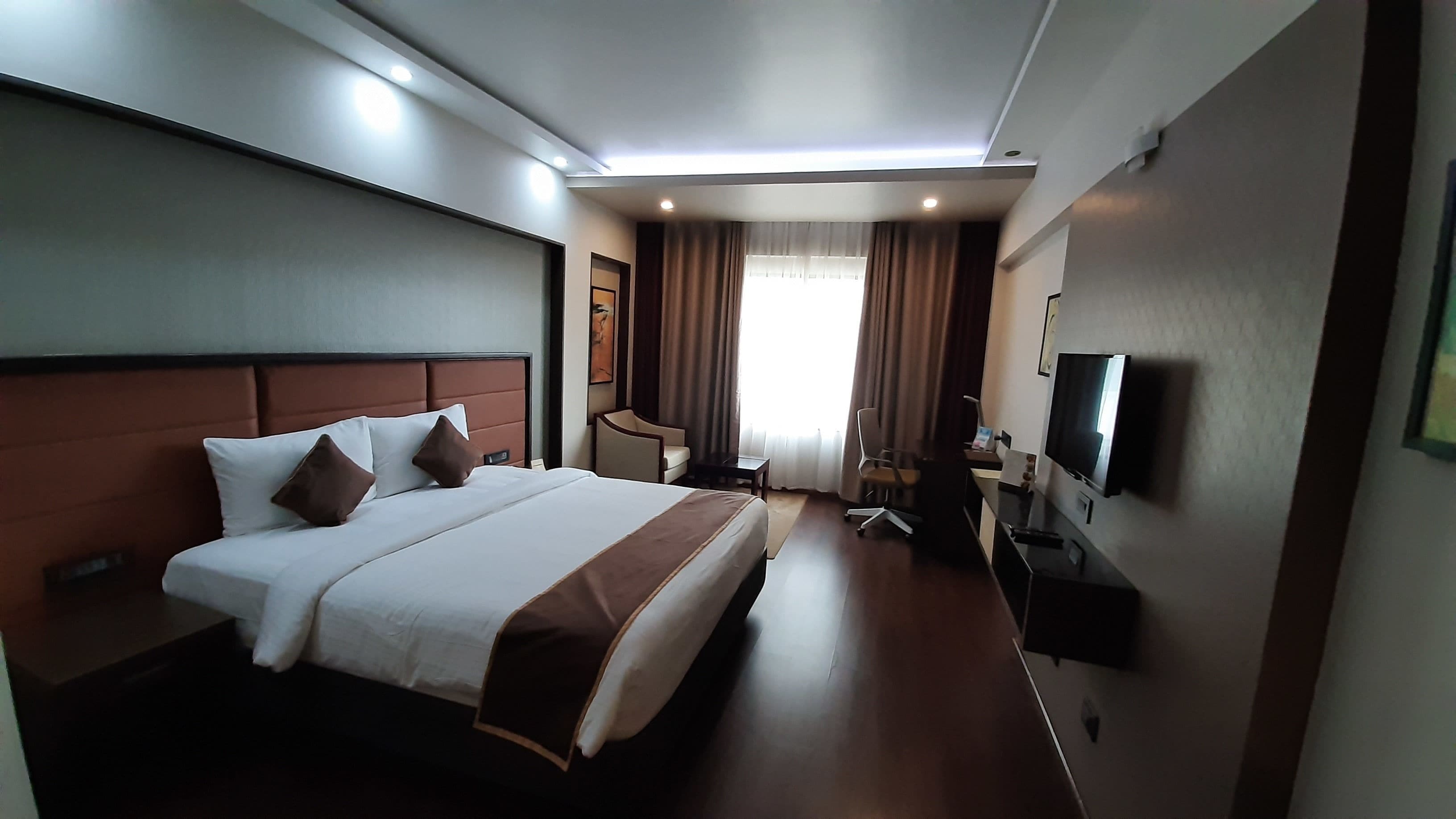 Una habitación de hotel con una cama grande, un escritorio, una silla, un televisor y una ventana con cortinas.