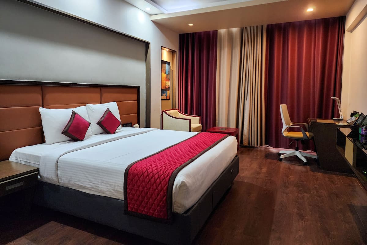 A hotel room with a large bed, a desk with a chair, and a desk lamp.