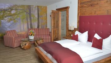 A bedroom with a large bed, striped armchairs, a glass coffee table, and a forest-themed wall mural.
