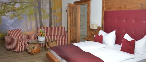 A bedroom with a large bed, striped armchairs, a glass coffee table, and a forest-themed wall mural.