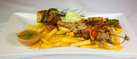 Un plato con brochetas de carne a la parrilla, papas fritas y un recipiente pequeño con salsa.